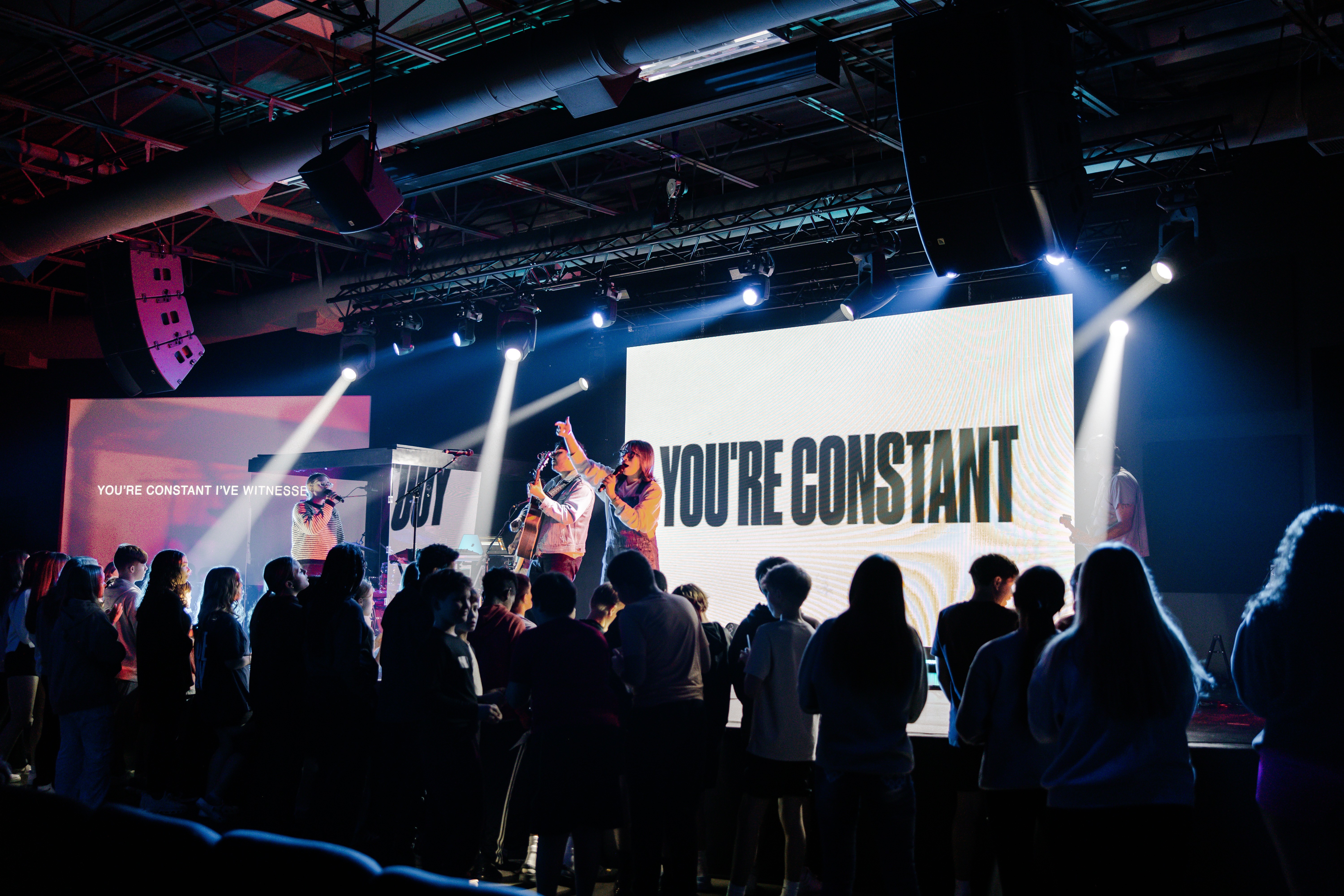 Audience members silhouetted against a bright stage with colorful lighting during an event or performance.