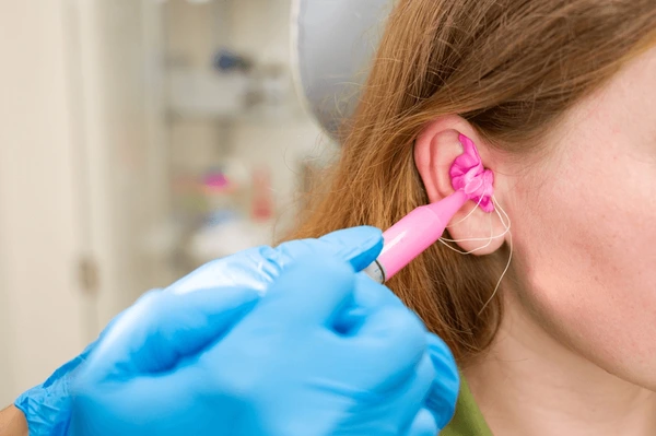 A close-up of a person getting an ear piercing with a pink tool, held by a gloved hand.