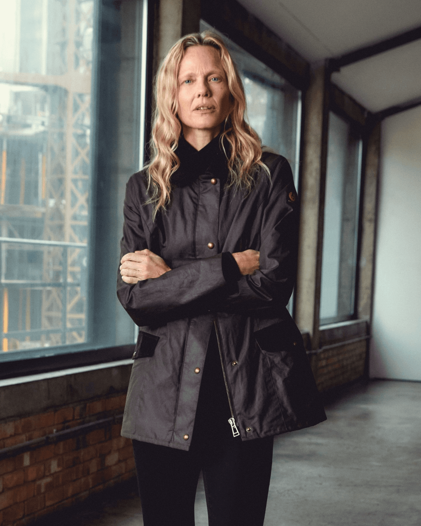 Une femme blonde porte une veste de moto en toile cirée Belstaff