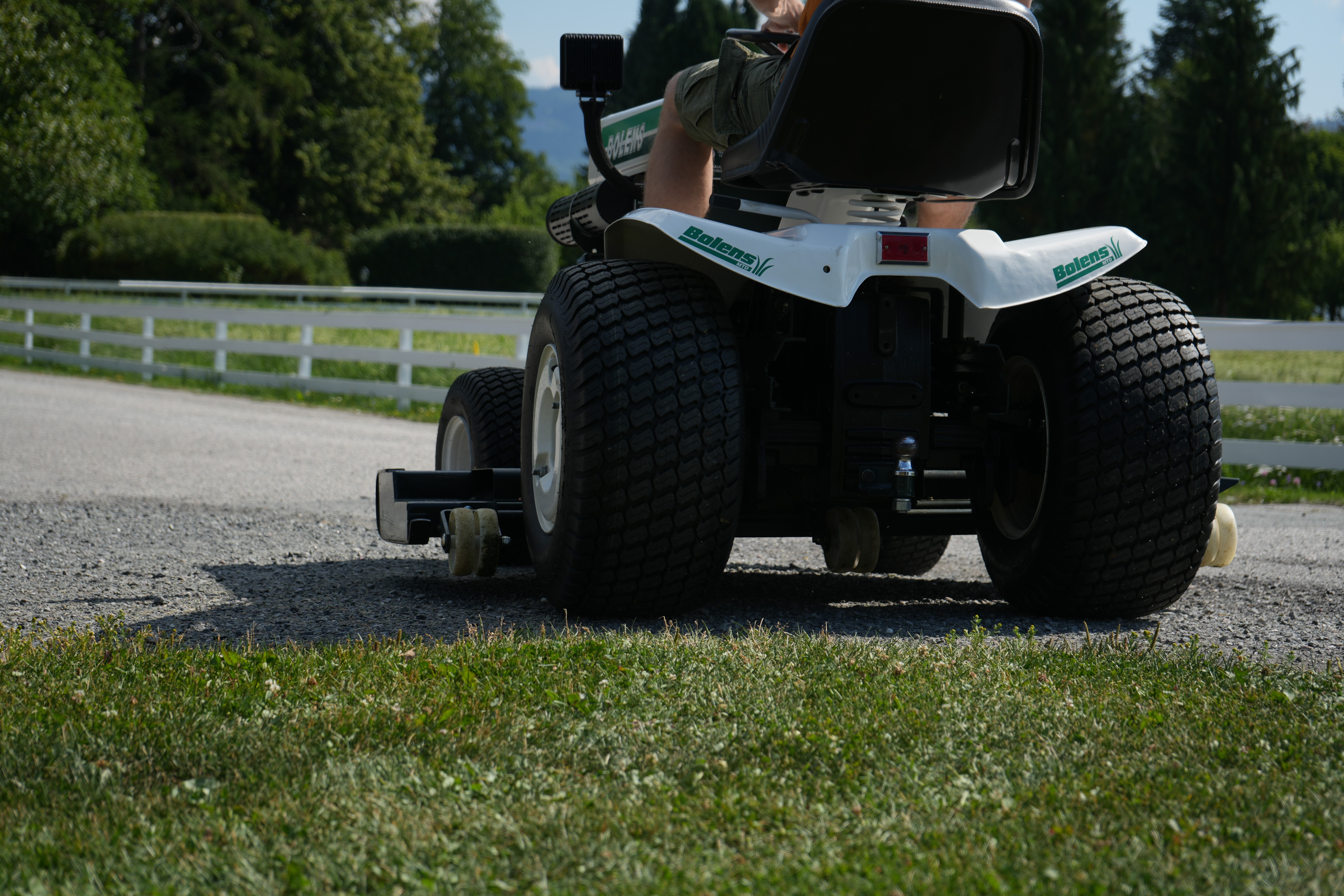 A spacious industrial-style interior with exposed brick walls, large windows, and natural light pouring in during sunset. Wooden desks with plants and workspace materials are arranged along the walls, with a view of greenery and an outdoor seating area.