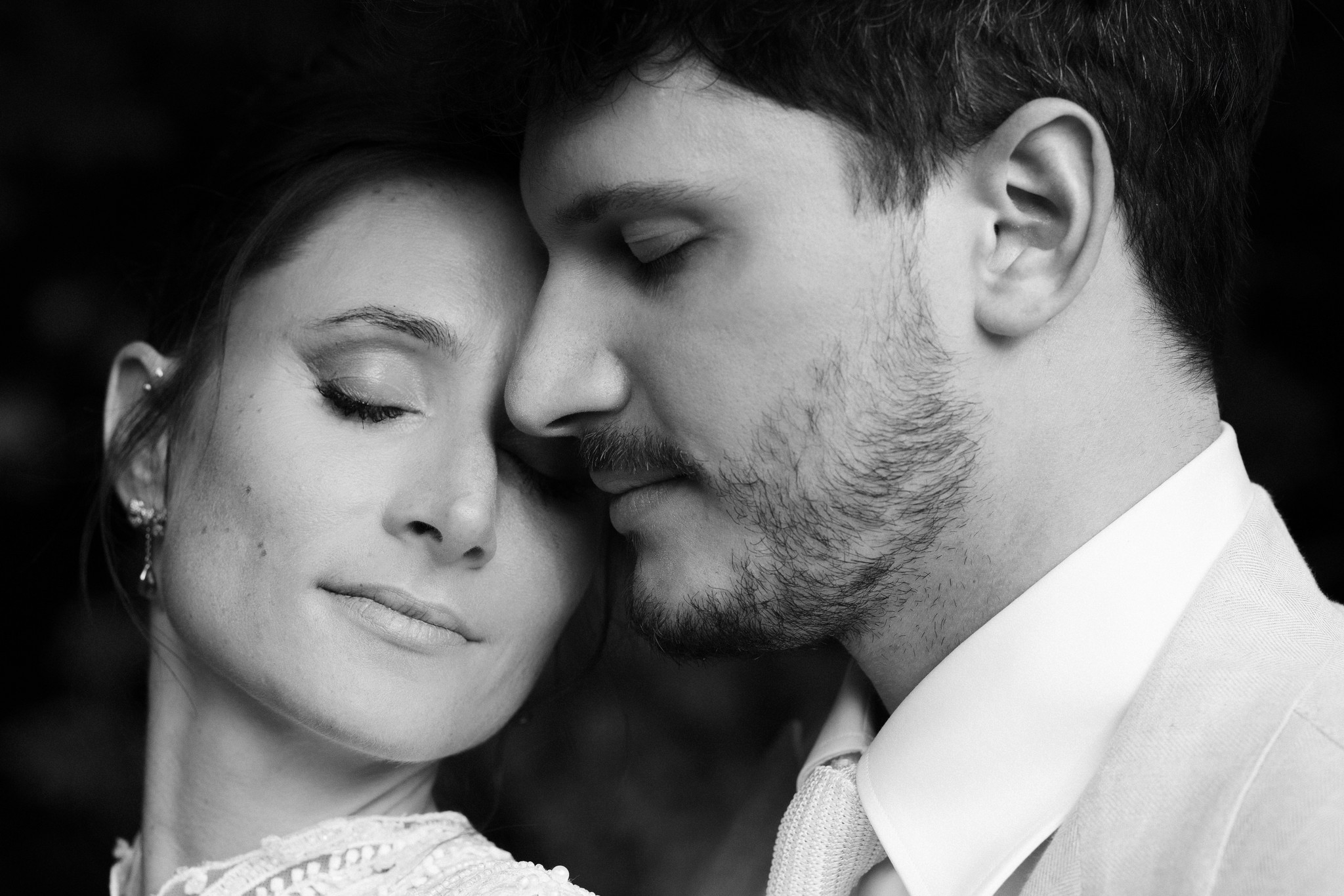 Sposi in primo piano, lei appoggiata a lui con occhi chiusi, lui che la bacia, ritratto di intimità dopo la cerimonia