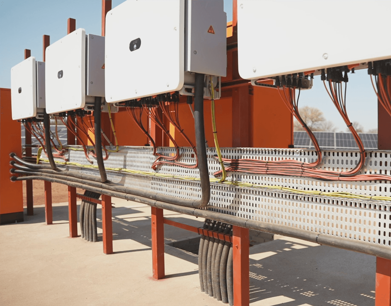 Modern two-story house with glass railings and stone facade, surrounded by desert landscaping. Prominent "For Sale" sign in the foreground under a clear blue sky.