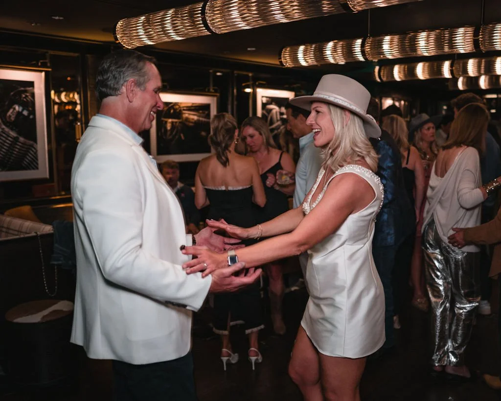 The bride and groom smile at each other and reach for each other's hands on the dance floor.
