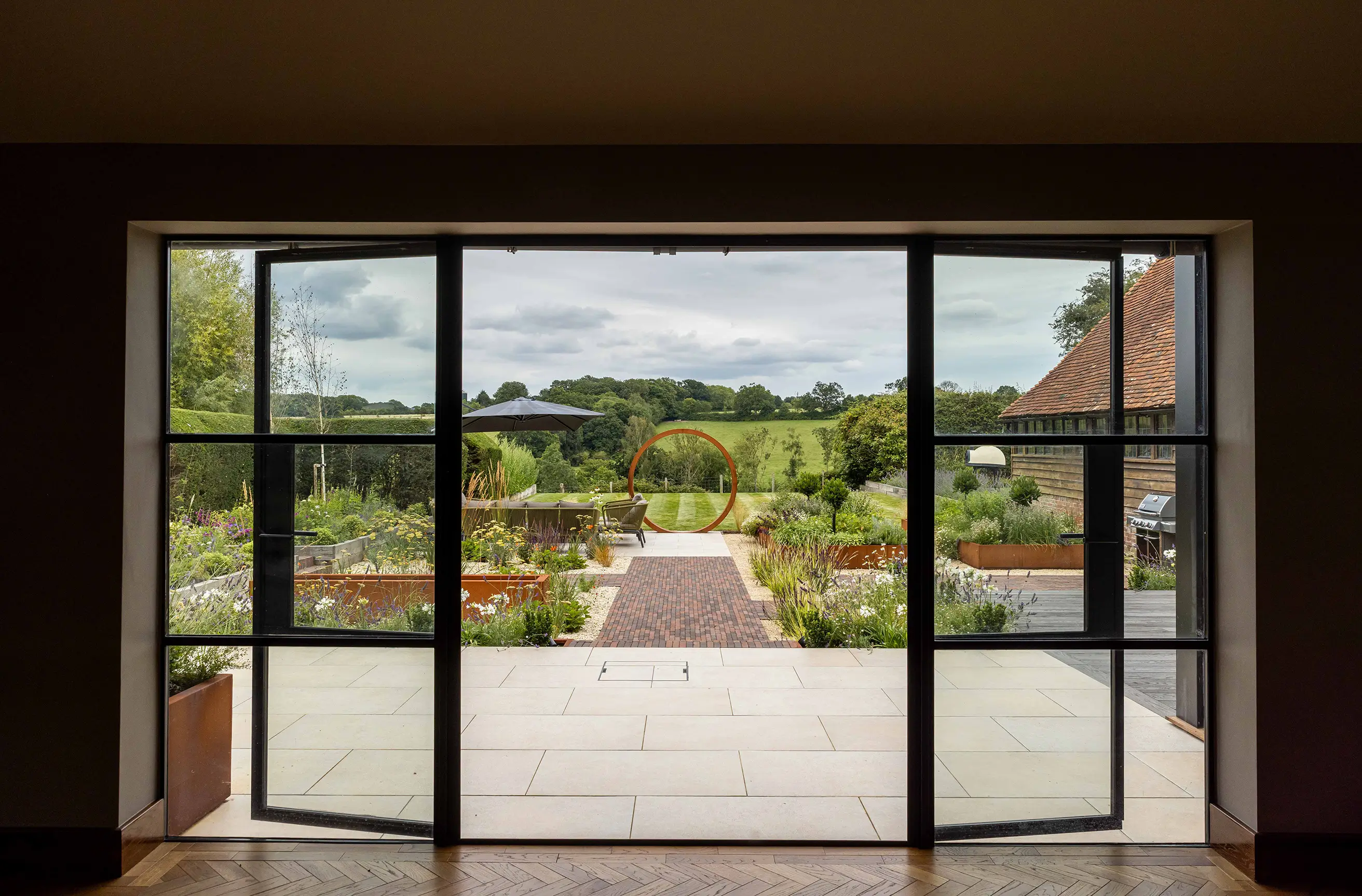 A modern glass door opens to a scenic landscaped garden with pathways and greenery.