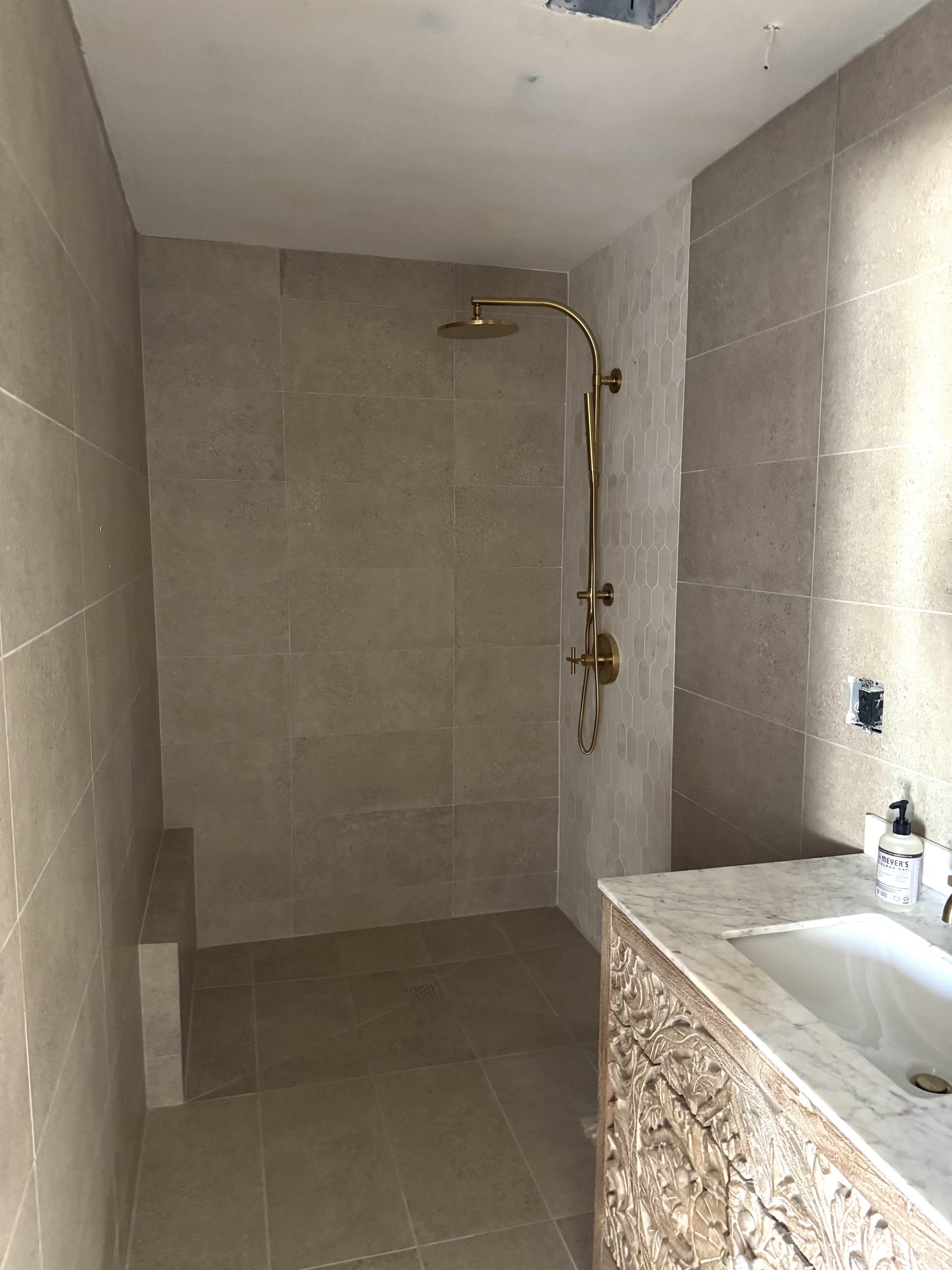 Custom bathroom shower with light brown natural stone wall and floor tiles, a built-in tiled bench, and brass shower fixtures.