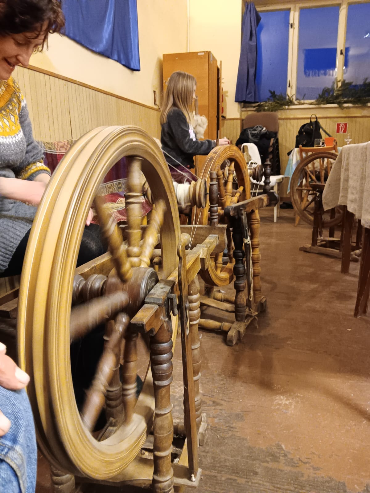 A smiling woman with her arms crossed, standing against a dark green background. She has long, dark hair.
