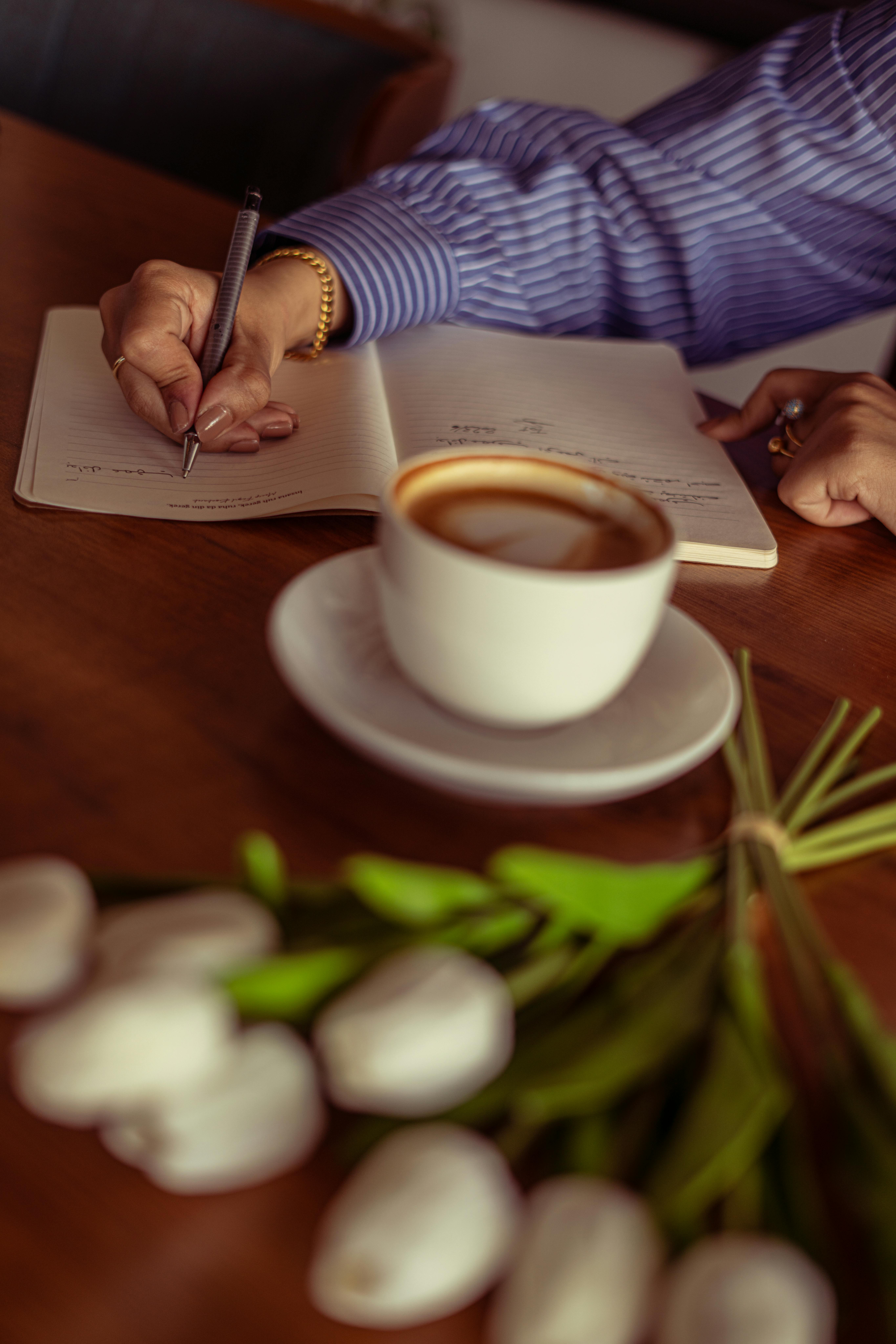 Una persona con una camiseta negra y pantalones de color claro está de pie en la cima rocosa de una montaña al atardecer, sosteniendo una cámara frente a su cara para tomar una foto. Un mar de nubes se extiende detrás de ellos, iluminado por la luz dorada del sol poniente.