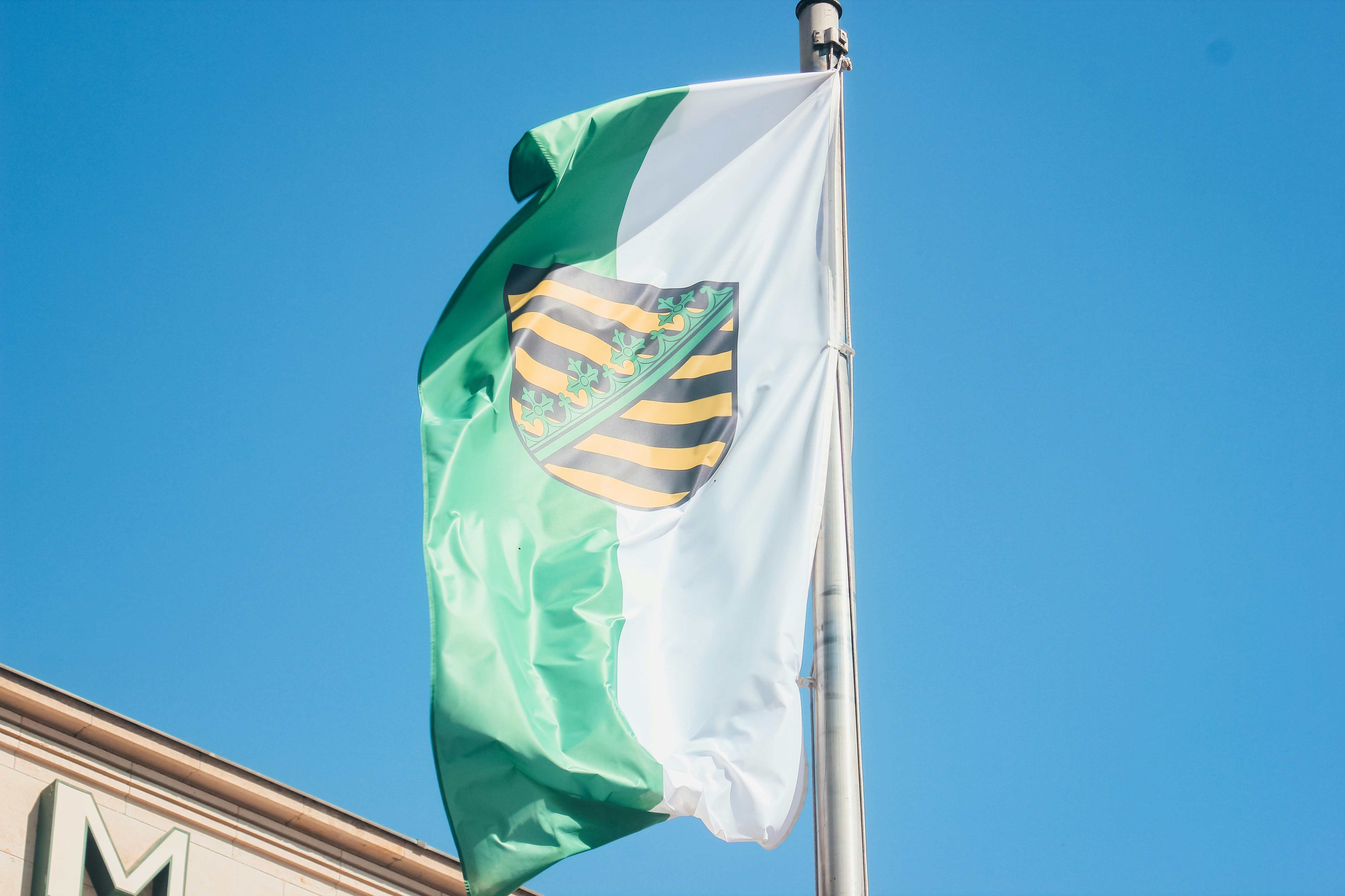 Flagge des Bundeslandes Sachsen mit grün-weißem Hintergrund und dem sächsischen Wappen in der Mitte.