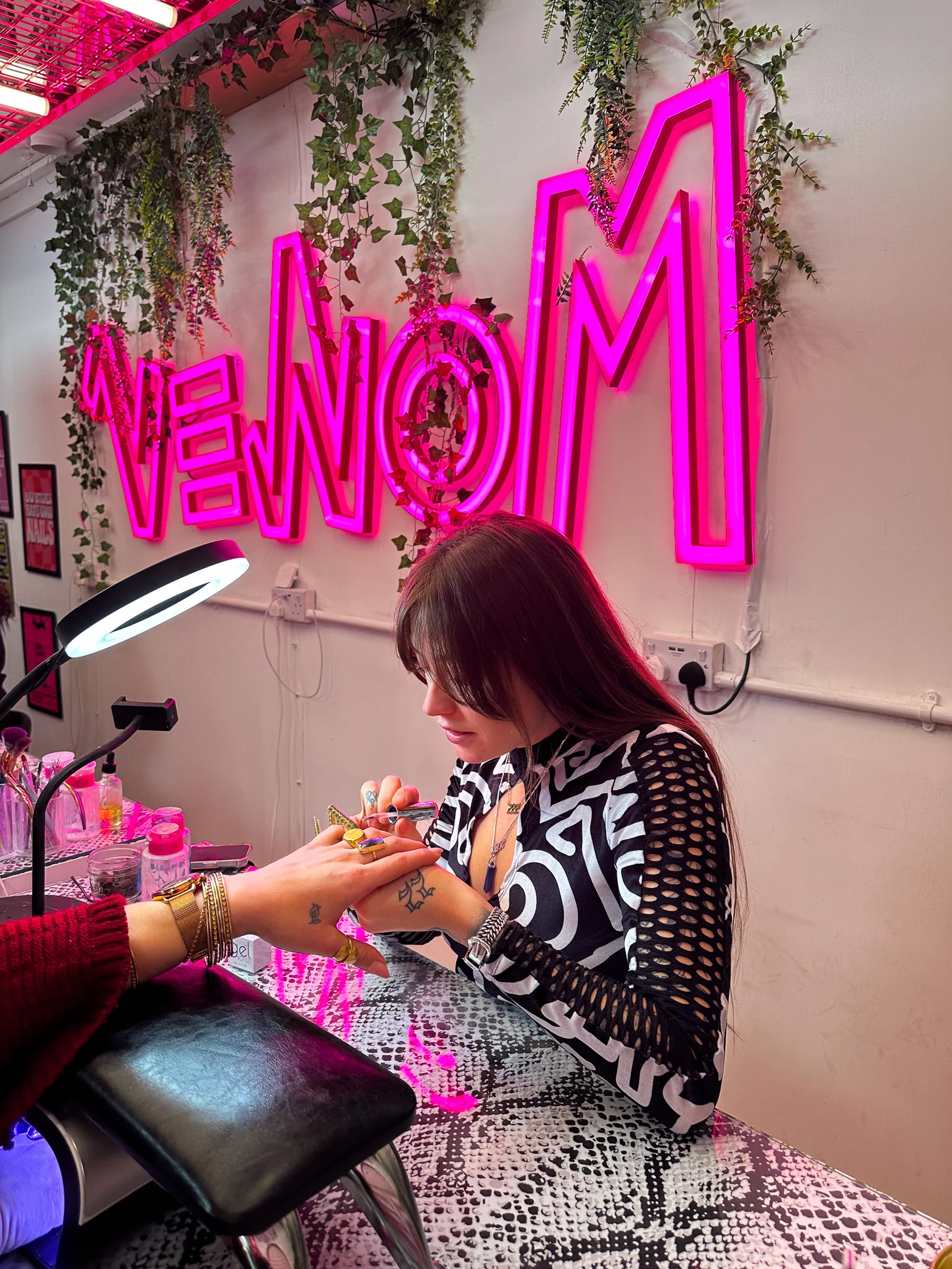 A top-down shot of a white round side table holding a book titled Fresh Sets: Contemporary Nail Art from Around the World and a small black card with the pink "VENOM" logo.