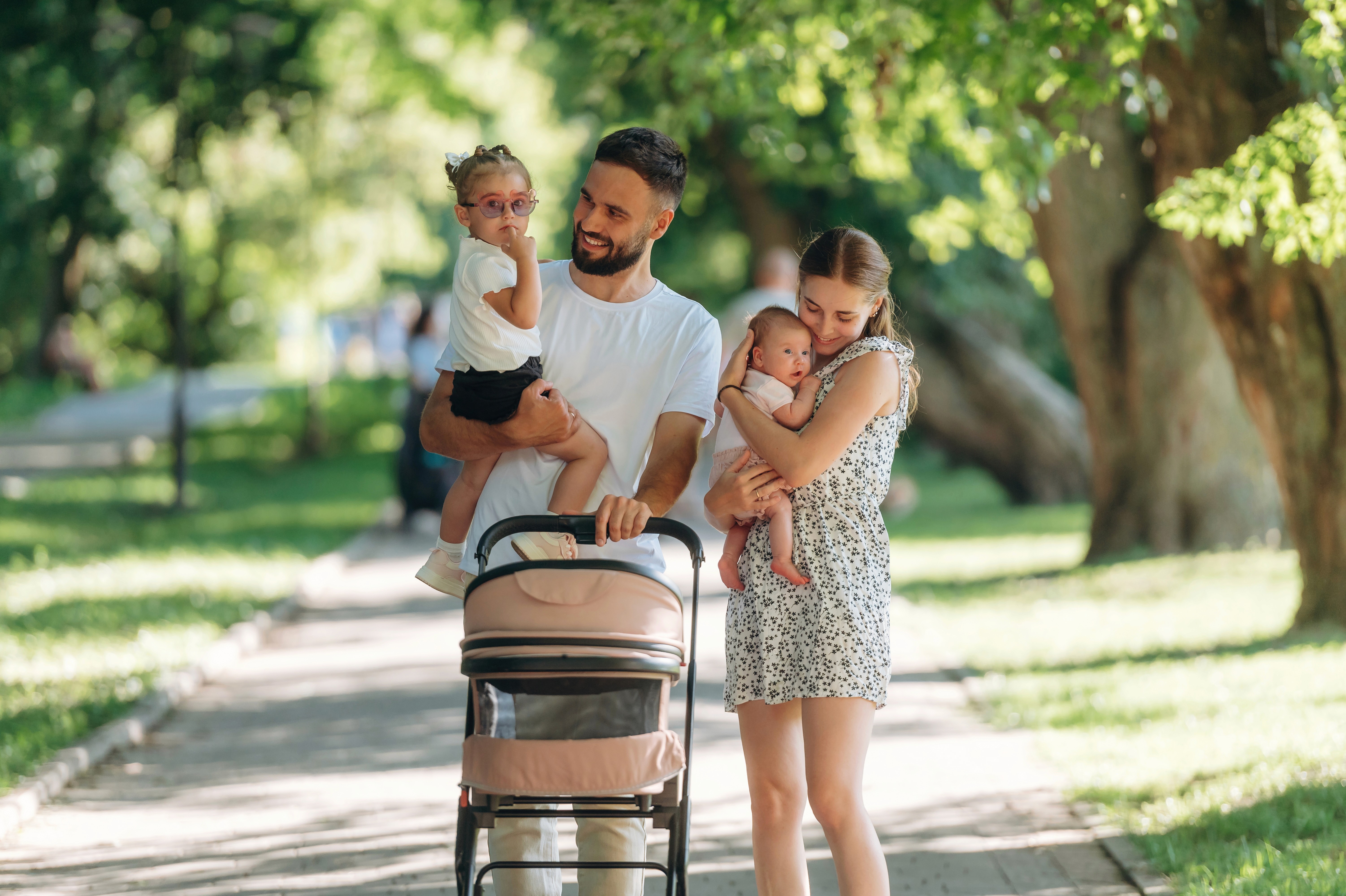 Familie mit Baby und Kinderwagen beim Spaziergang im Park – Unterwegs mit Baby und wichtiger Teil der Erstausstattung.