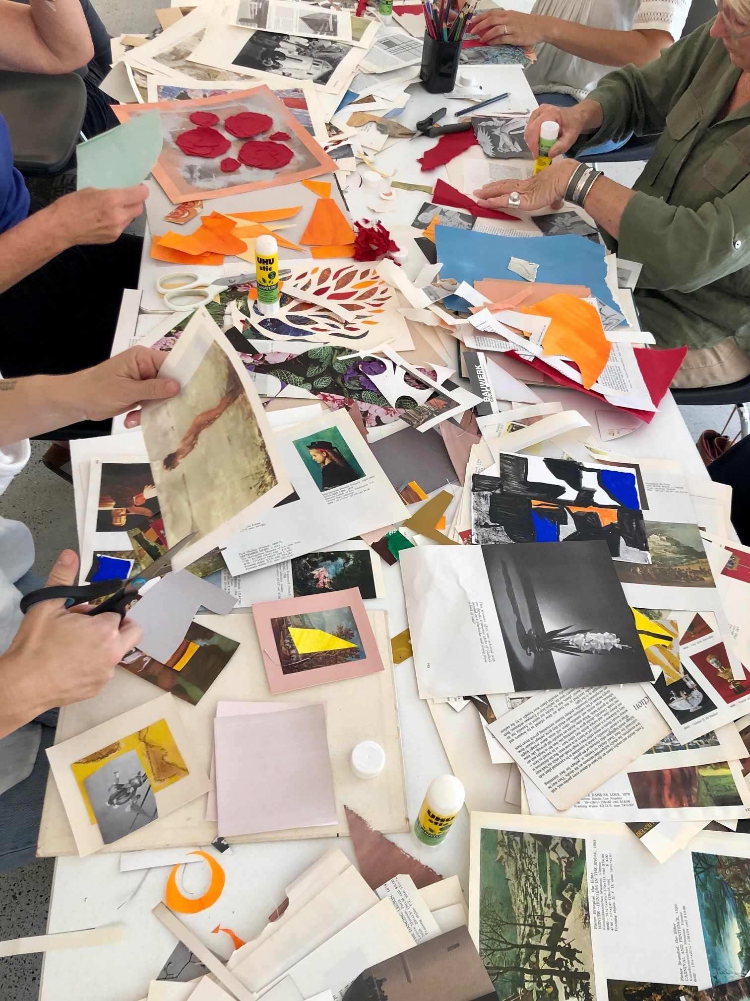 Overhead view of hands working on collage materials spread across a shared table