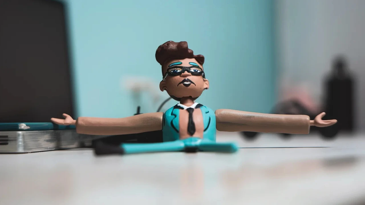 Figurine stylisée représentant un personnage en costume turquoise avec lunettes de soleil, bras ouverts à l’horizontale, posée sur un bureau devant un ordinateur. L’image illustre la question de la diversité en entreprise, entre posture affichée et véritable stratégie d’inclusion.