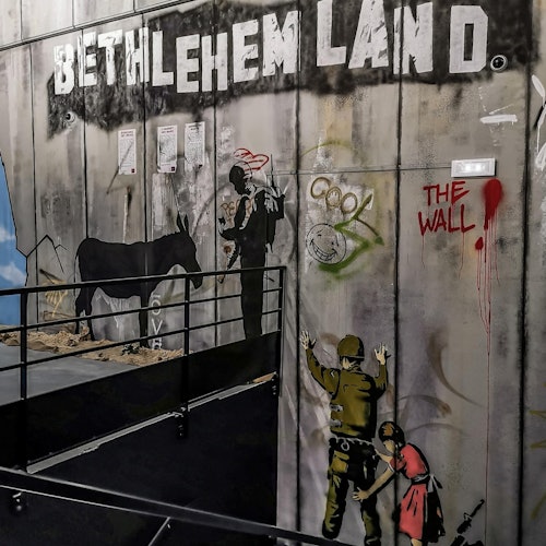 墙上的涂鸦展示了士兵、一只驴和孩子们。大字写着“伯利恒之地”和“城墙”。