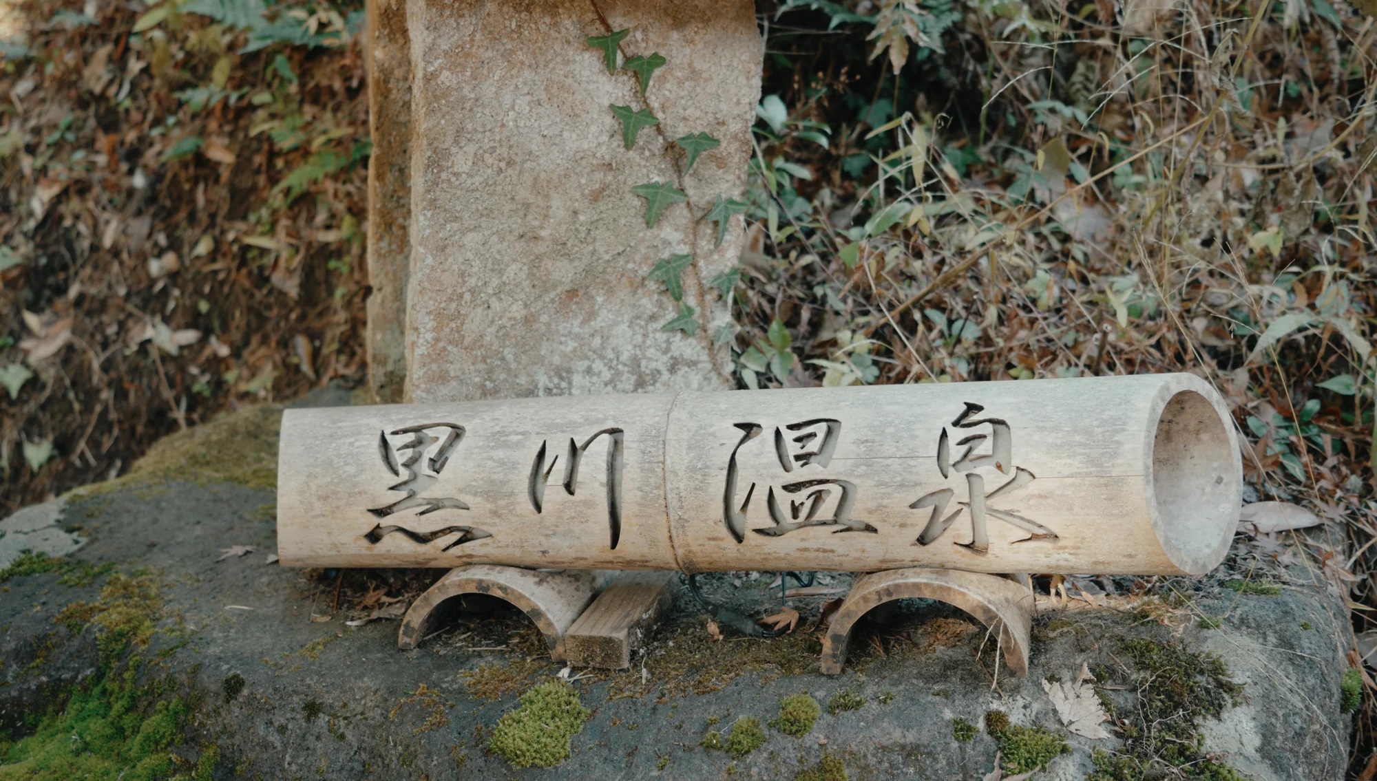 A weathered stone marker carved with the name Kurokawa Onsen against a mossy wall