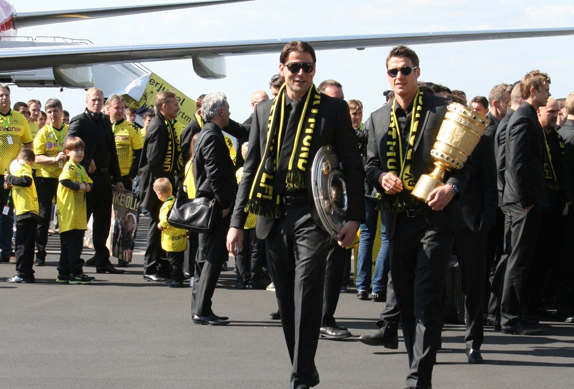 BVB-Spieler tragen Meisterschale und DFB-Pokal über das Rollfeld