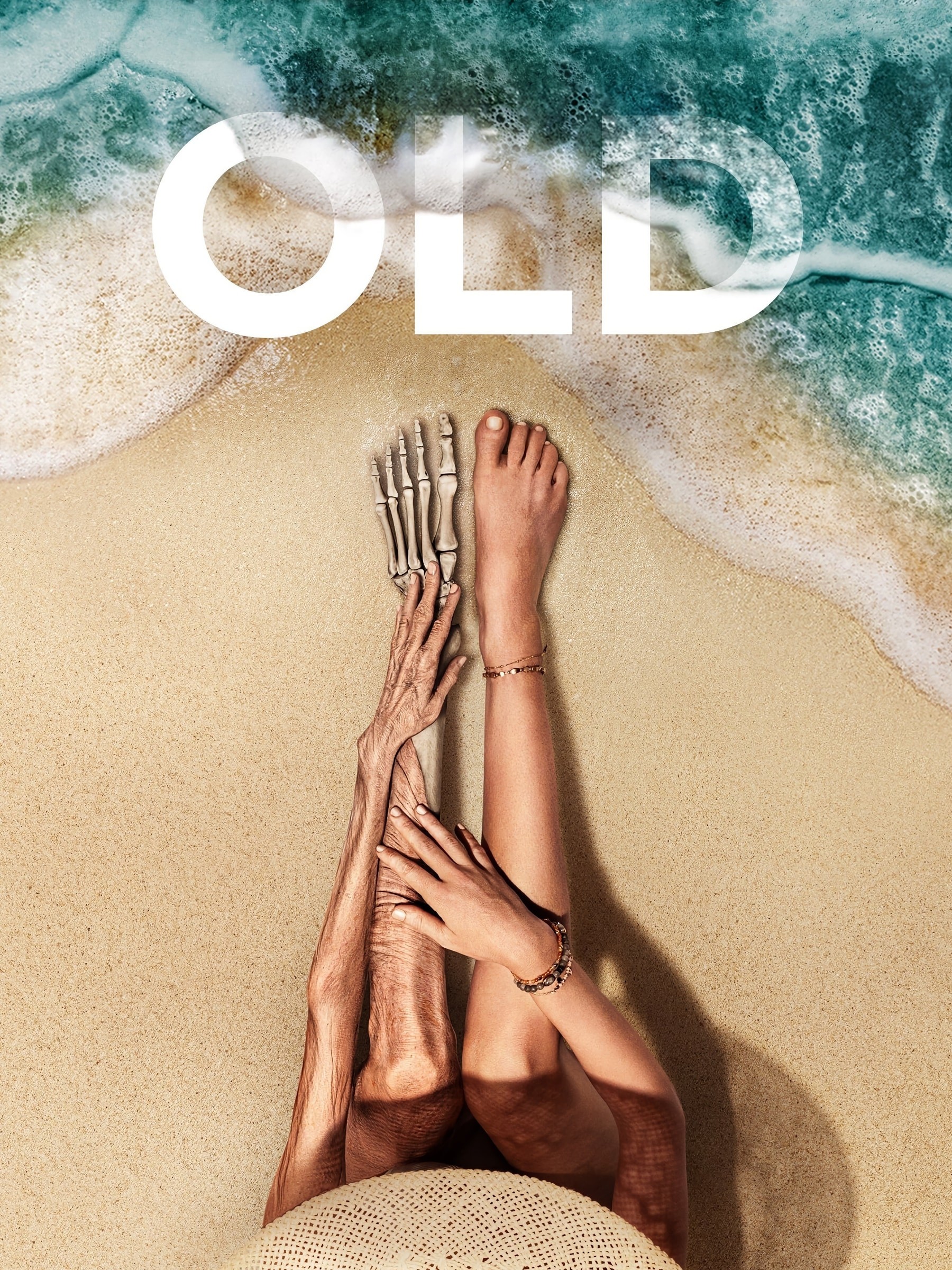 Movie poster showing a woman’s legs on sand, one normal and one aged to bone, with ocean waves and the title “Old.”
