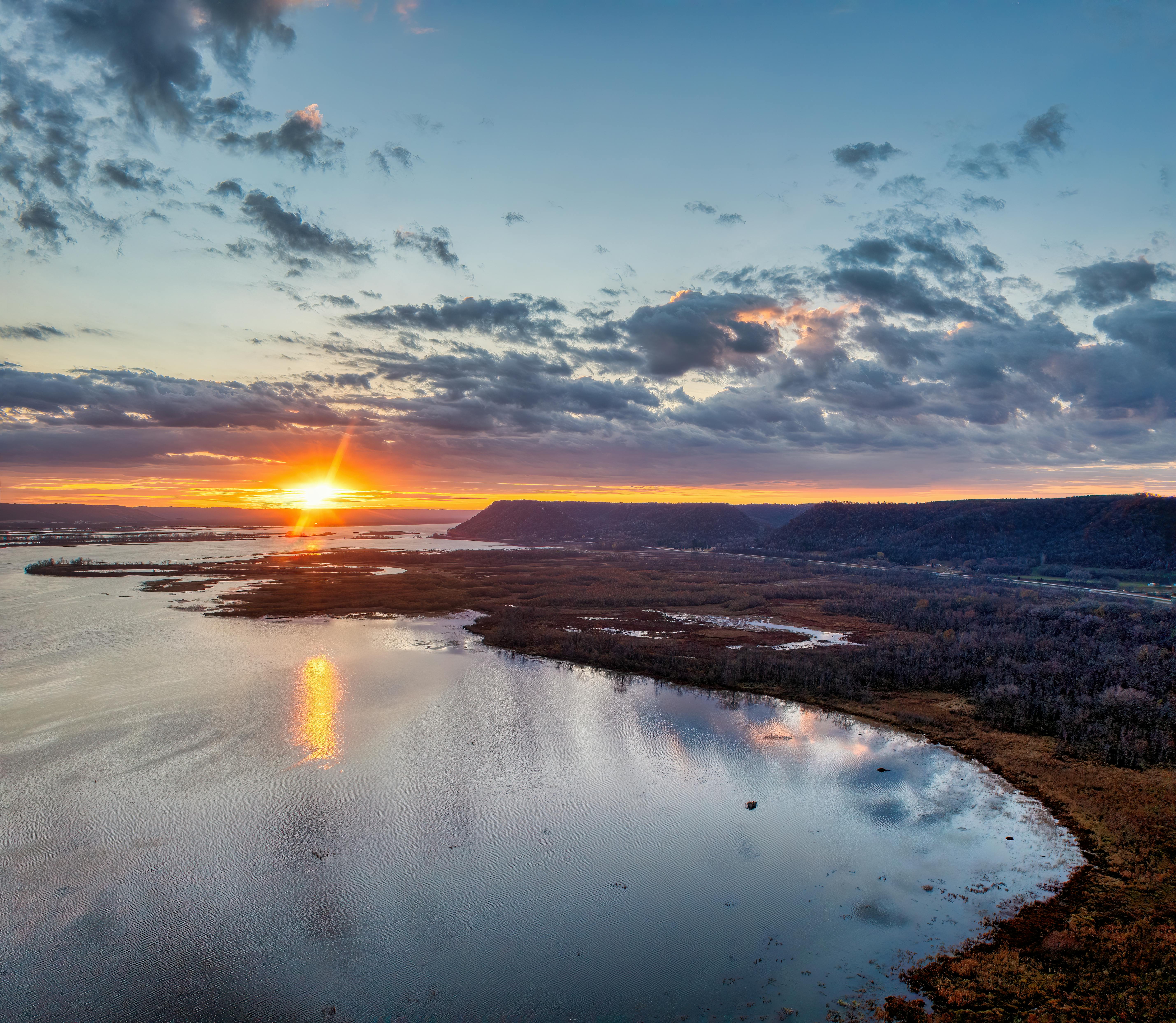 Sunset over a wide river with distant hills and dramatic clouds