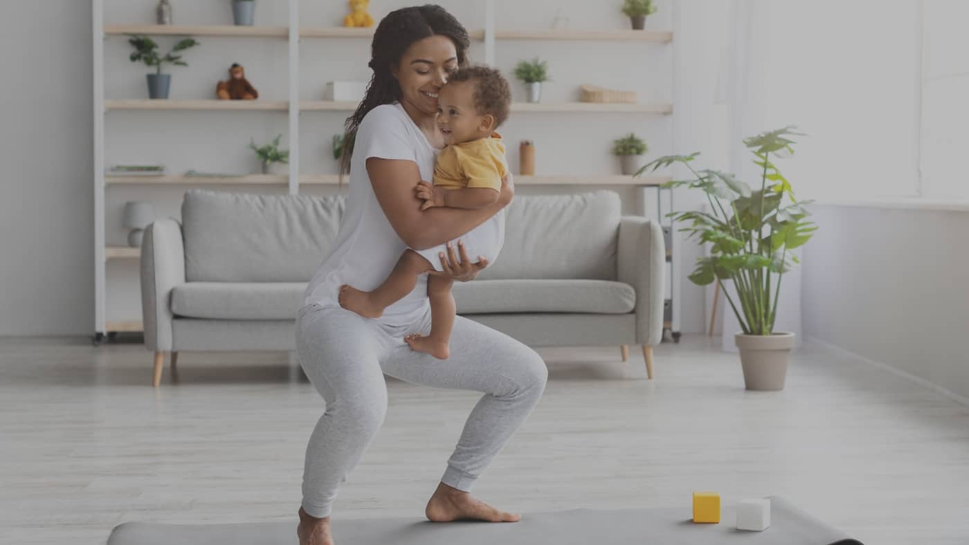 Jeune maman en post-partum effectuant une séance de renforcement musculaire doux à domicile avec son bébé blotti dans ses bras.