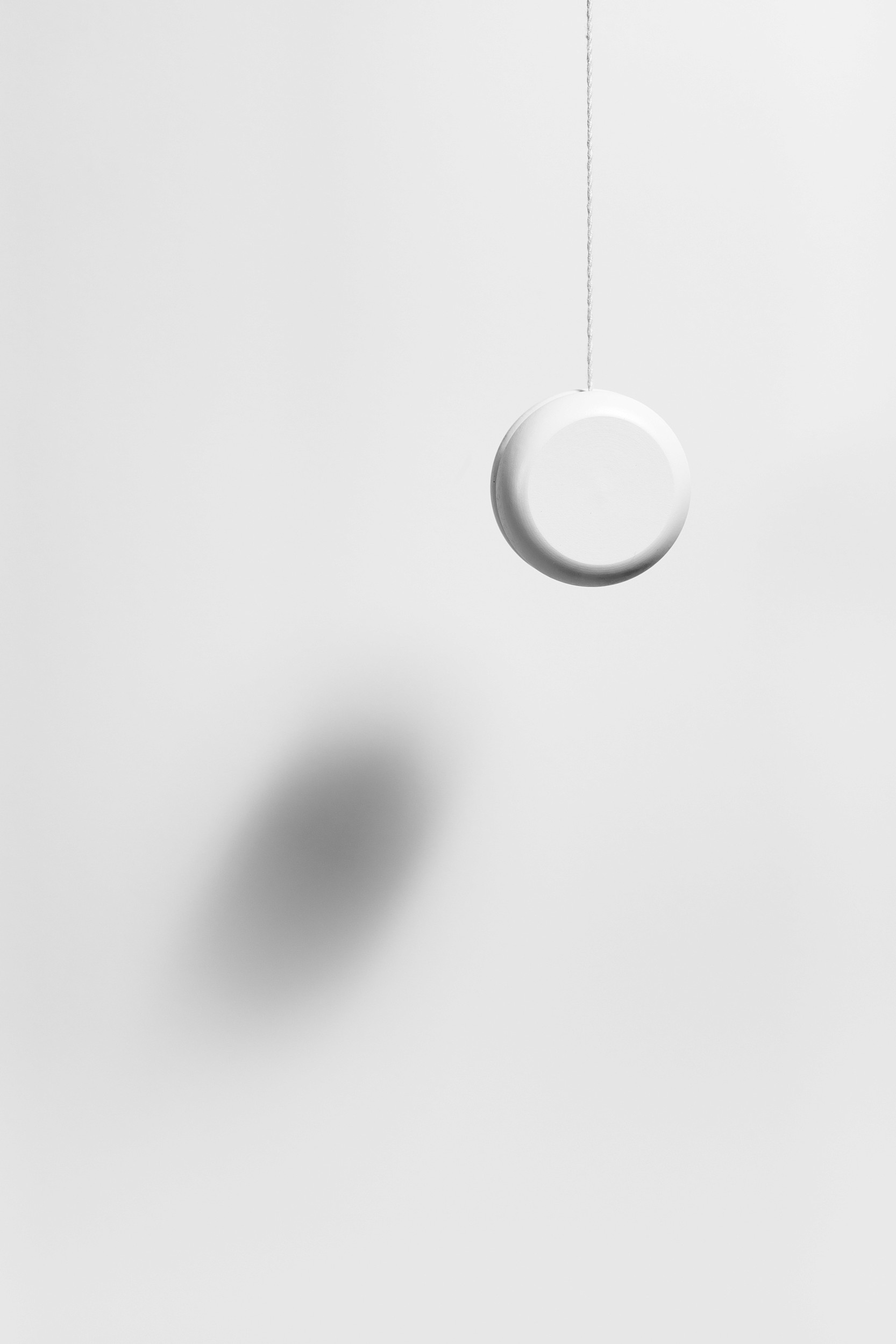 Minimal photograph of a yo-yo hanging from its string against a soft white background.
