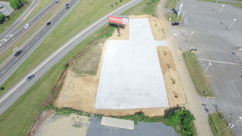 Overhead drone shot of vacant log with gravel base with road on one side with cars on it.