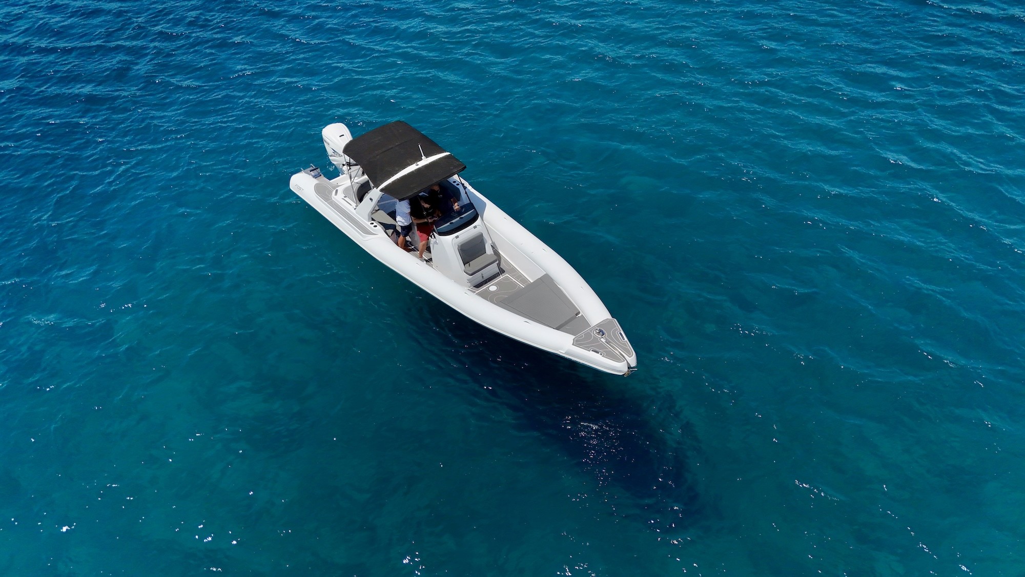 White Fost Matrix 32 rigid inflatable boat with black T-top canopy anchored in crystal-clear turquoise waters of the Aegean Sea.