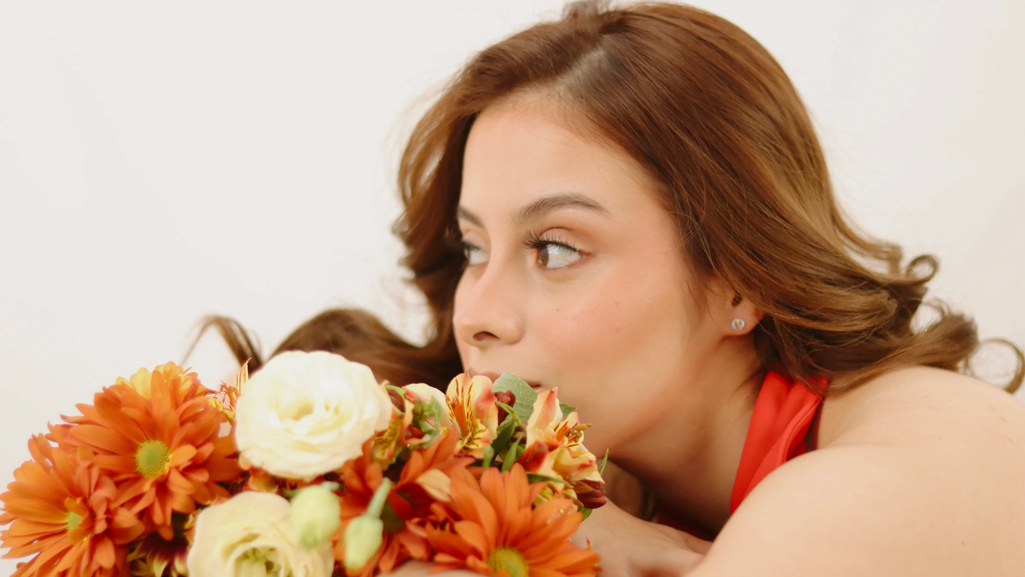 Retrato femenino con flores naranjas cerca del rostro y fondo blanco
