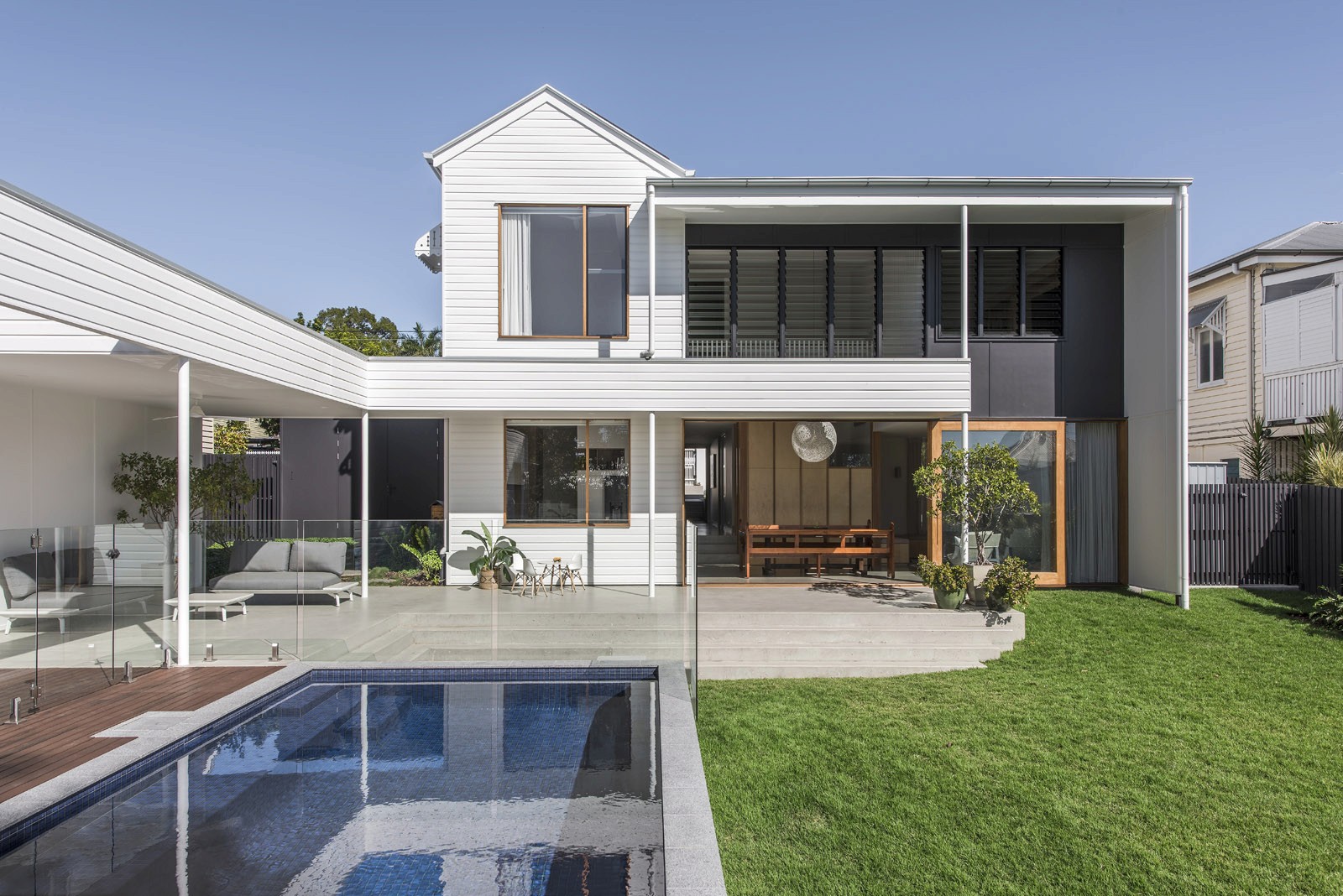 Rear elevation of modern residential house with outdoor pool, lawn, and open-plan living area