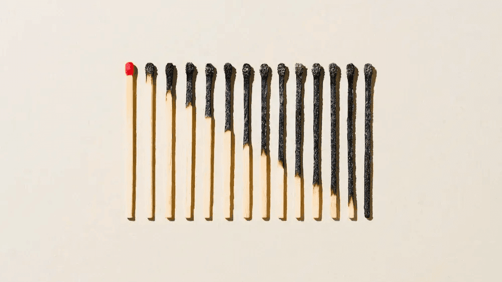 A row of burned matches beside a single unlit match with a red tip, symbolizing burnout and the potential for renewal.