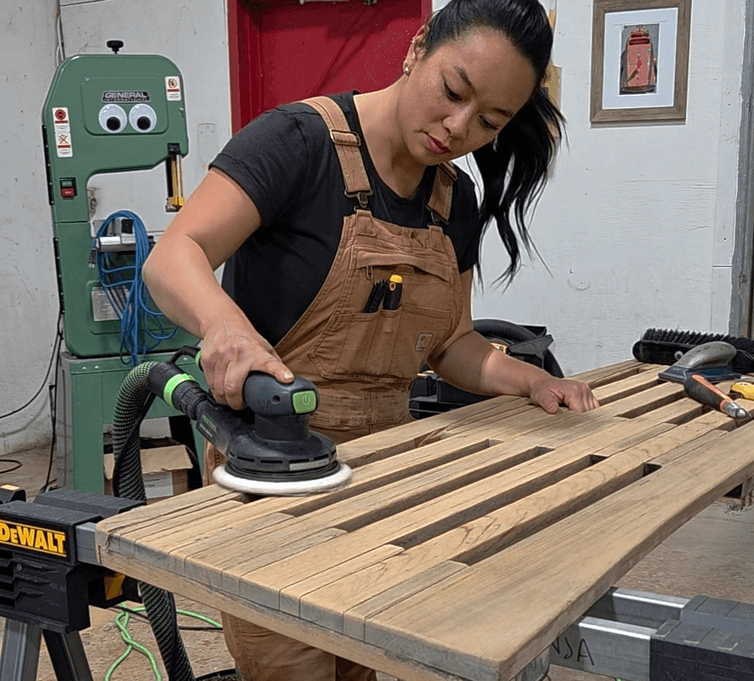 A woman sanding the teak platform of a boat to restore it