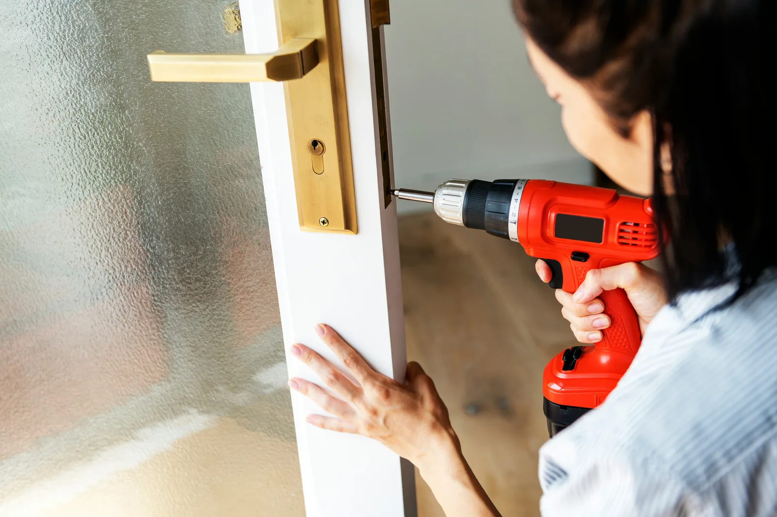 Woman using power drill to install brass door handle hardware