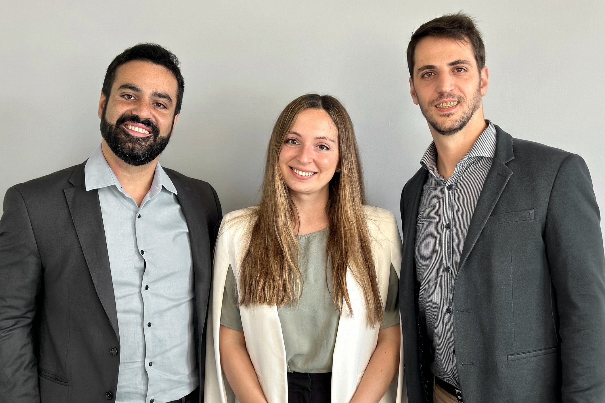 Three founders smiling warmly, standing together against a plain background.