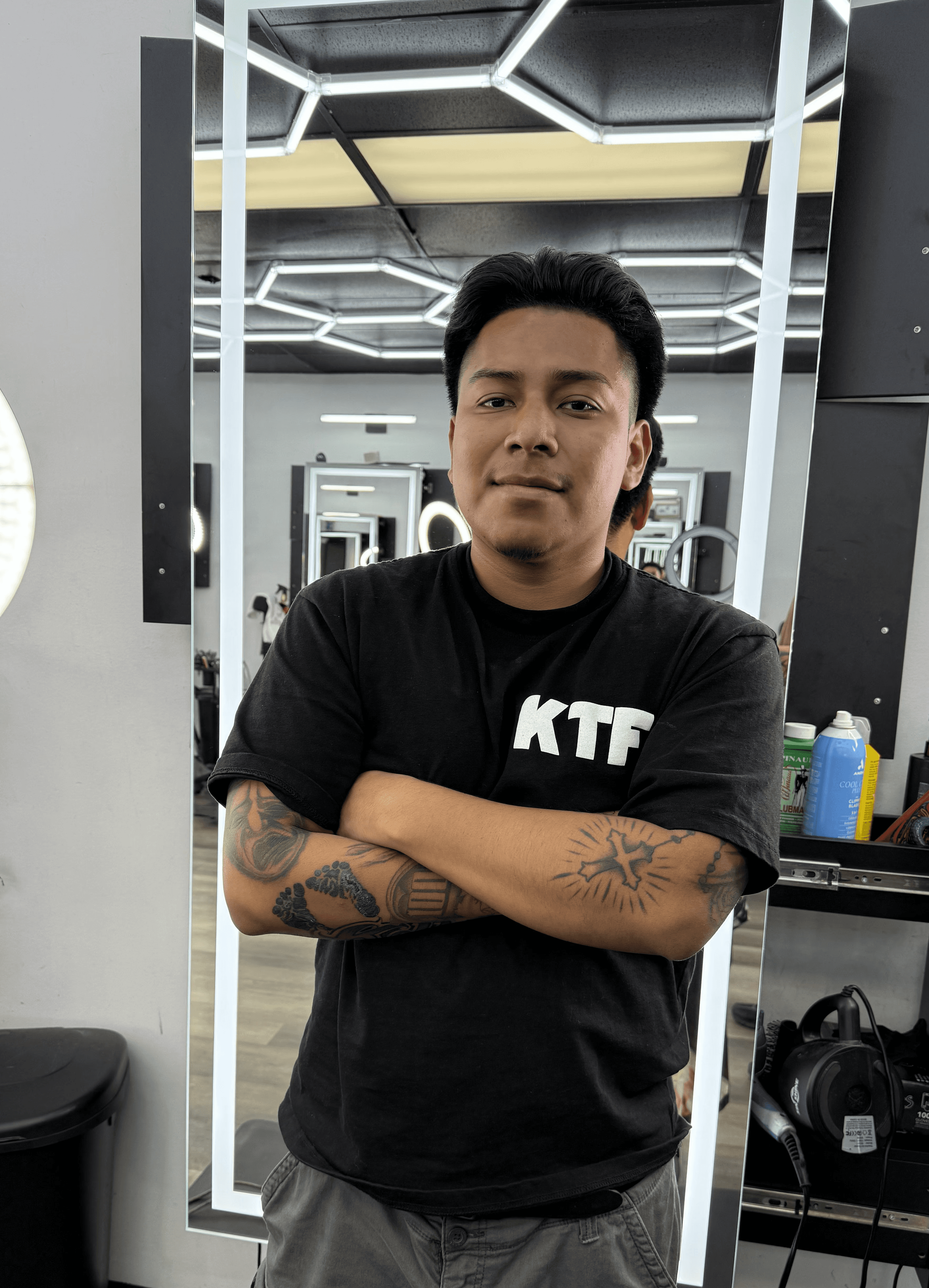A barber shapes a client’s haircut using clippers near a bright ring light in barbershop. 