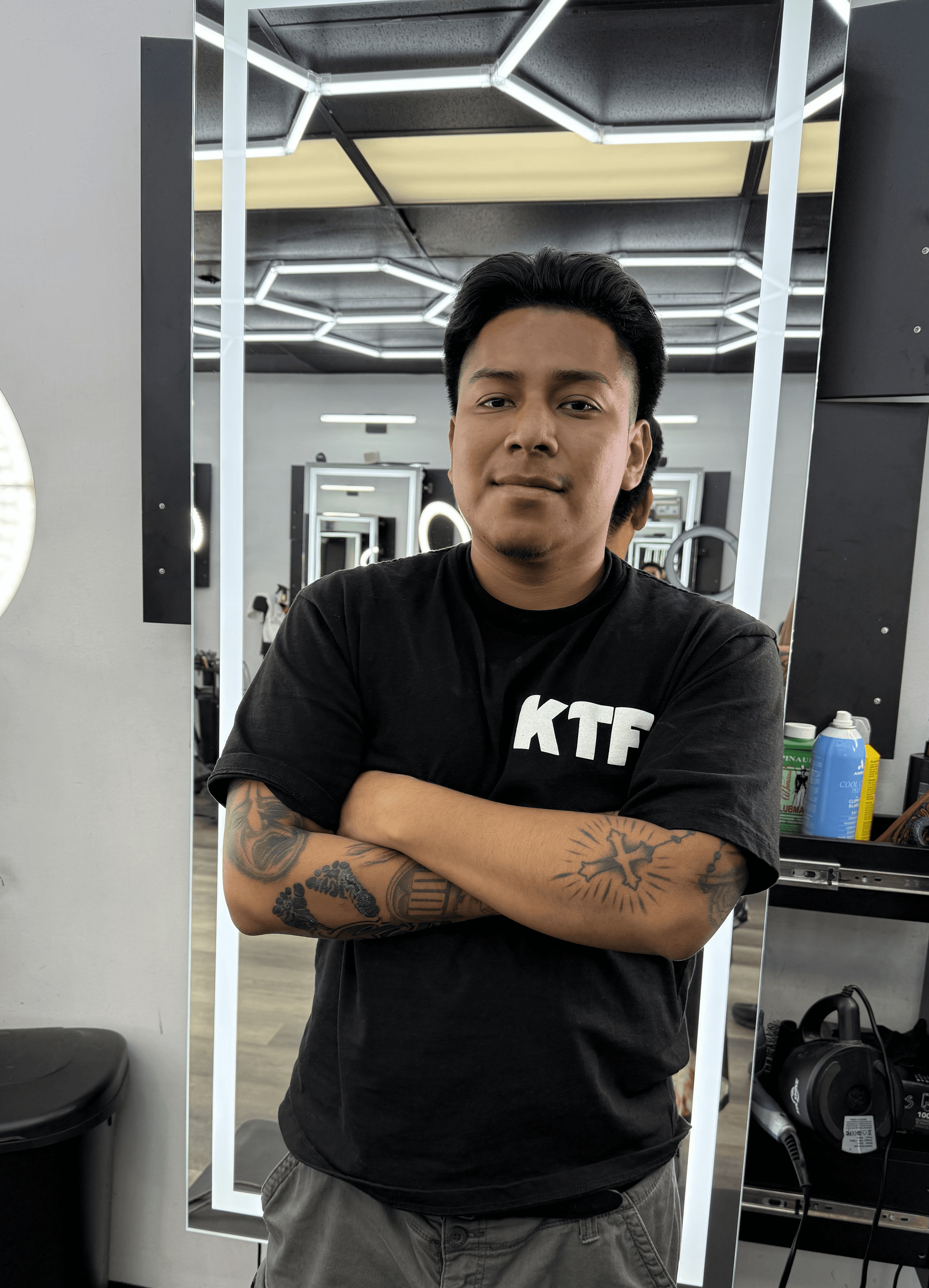 A barber shapes a client’s haircut using clippers near a bright ring light in barbershop. 