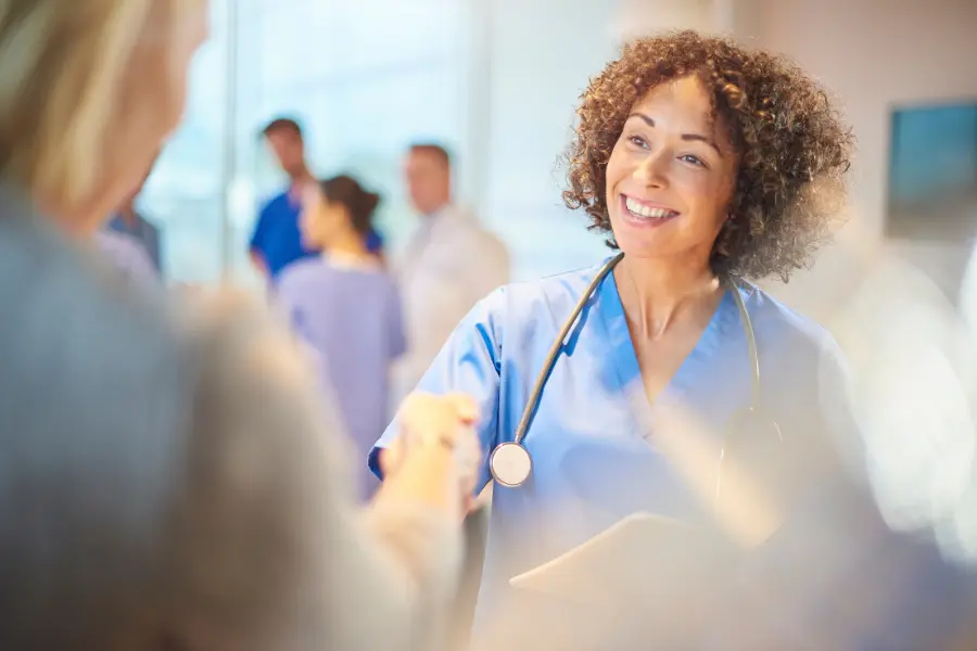 AI medical billing and coding in practice as a smiling nurse with a stethoscope shakes hands with a patient in a busy hospital setting.