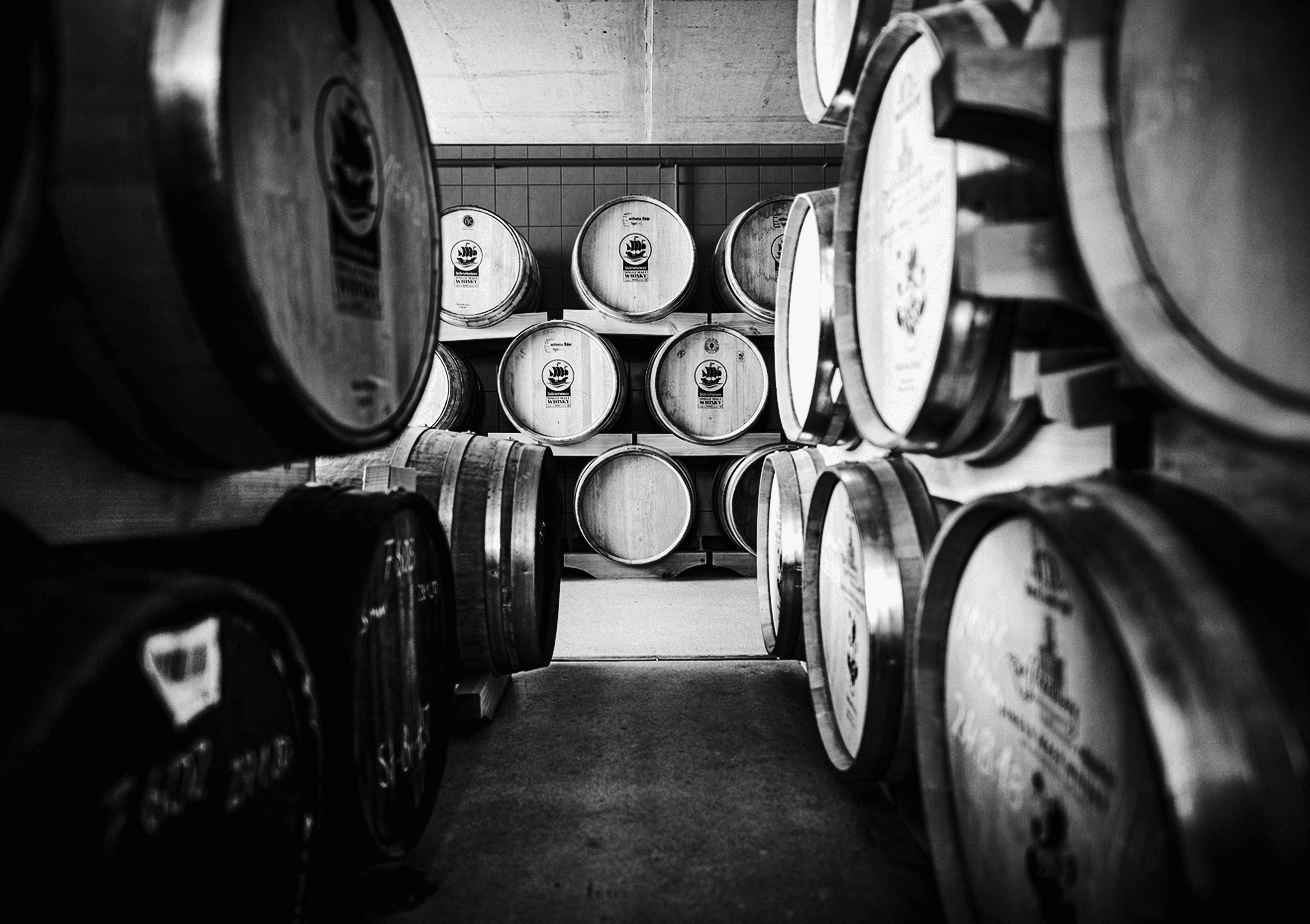 Whiskey barrels stacked in a cellar, black and white.