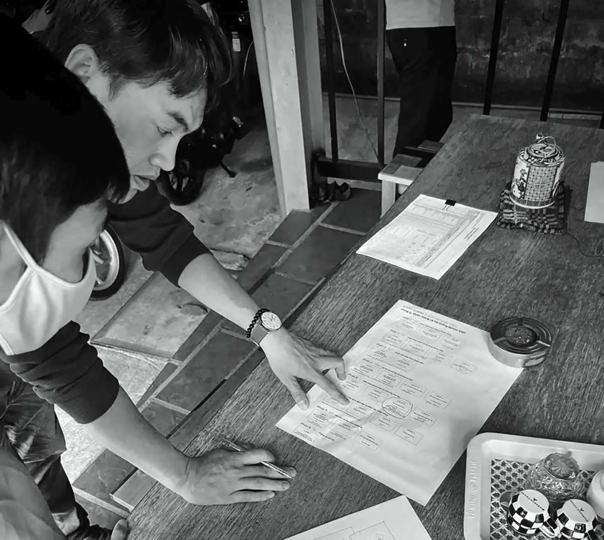 Black and white photo of two people looking at a computer screen with papers on wall