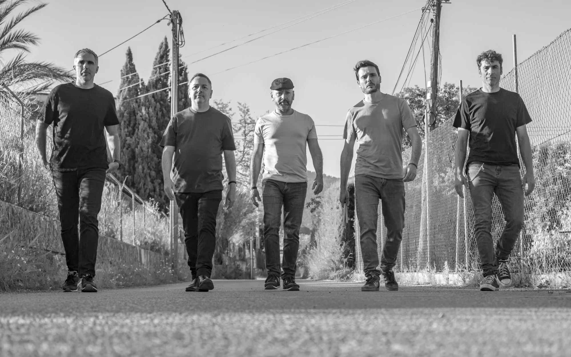 Los cinco integrantes de Breaking Silence caminan hacia la cámara por un camino rural, en blanco y negro.