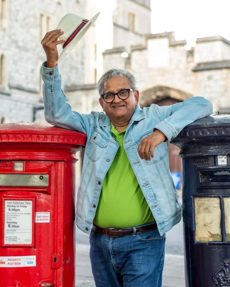 Rajesh Nagjee relaxed and playful between two London post boxes, tipping his hat — the side of leadership that doesn't show up in boardrooms.