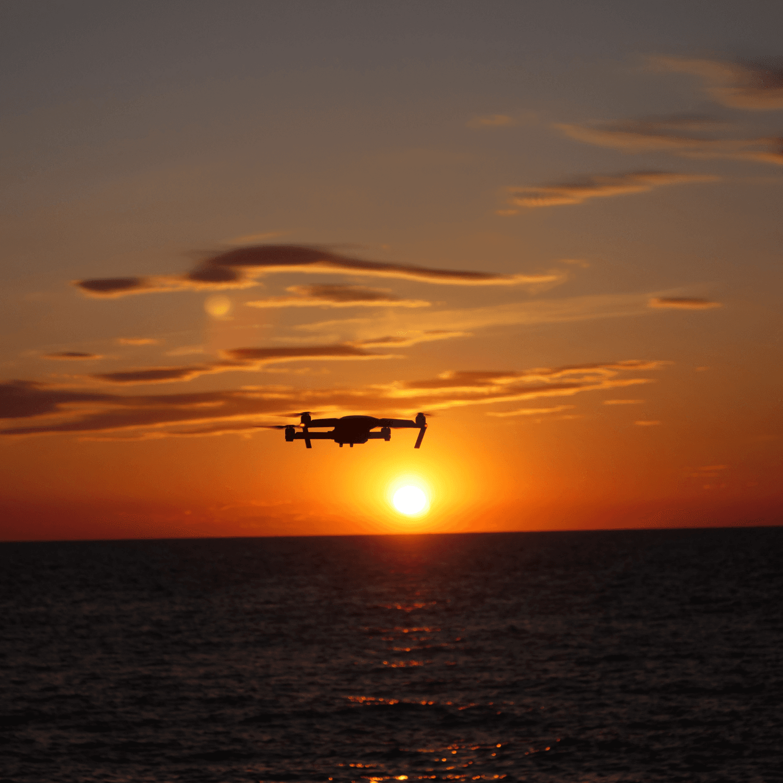 An image of a DJI Mini 4 Pro drone flying over the sea towards the sunset.
