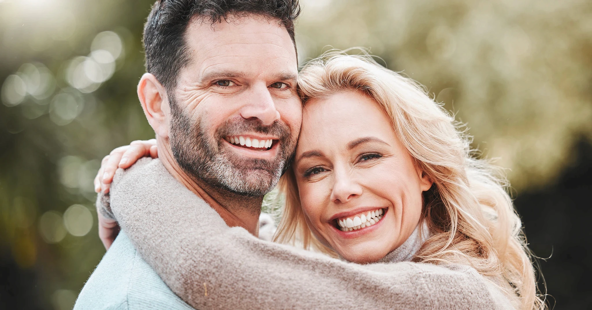En lycklig man och kvinna omfamnar varandra och ler brett medan de ser direkt in i kameran, utstrålande glädje och nära anknytning i ett romantiskt förhållande.