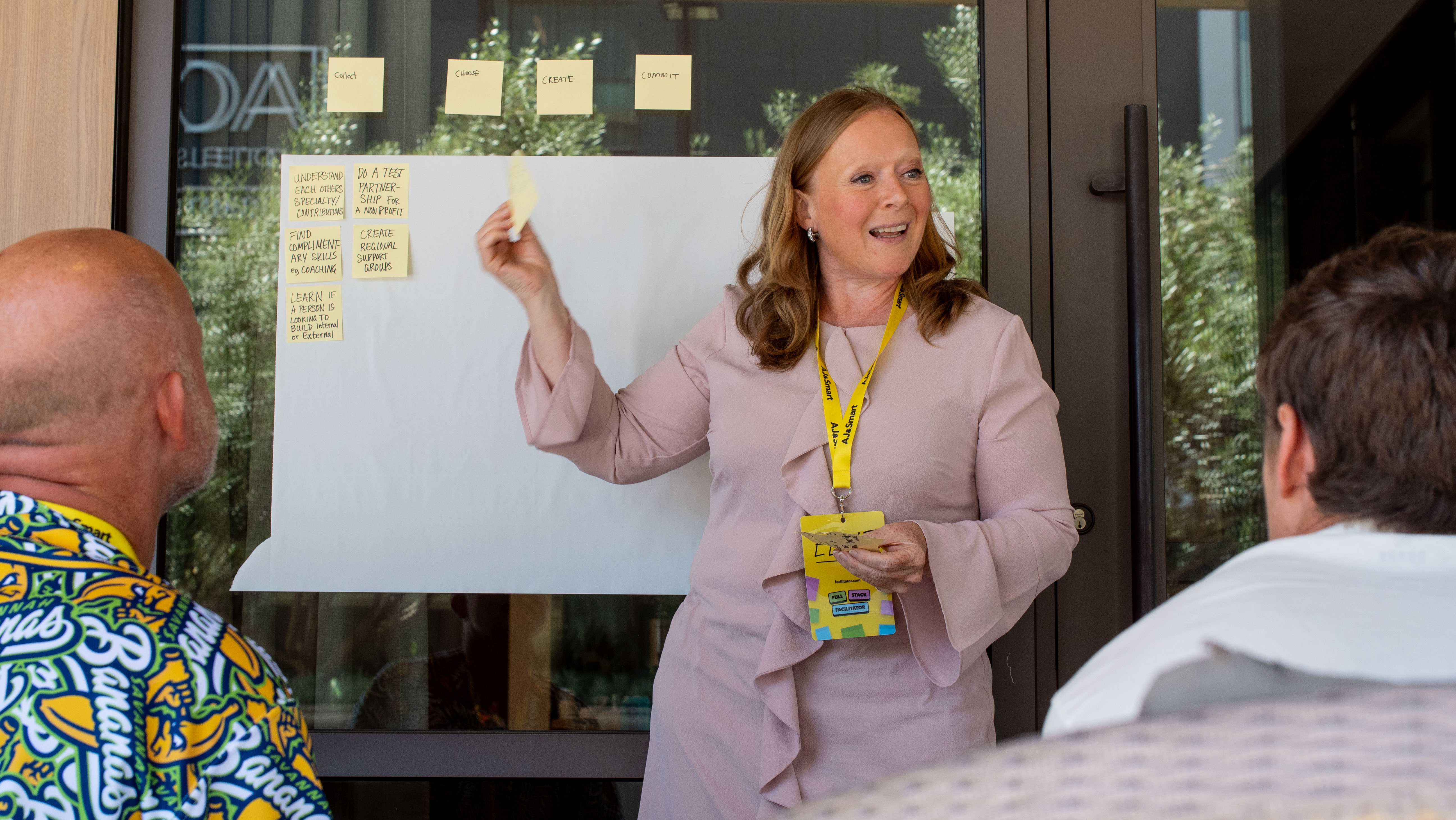 Professional facilitator placing sticky notes on a whiteboard while presenting workshop exercises to participants