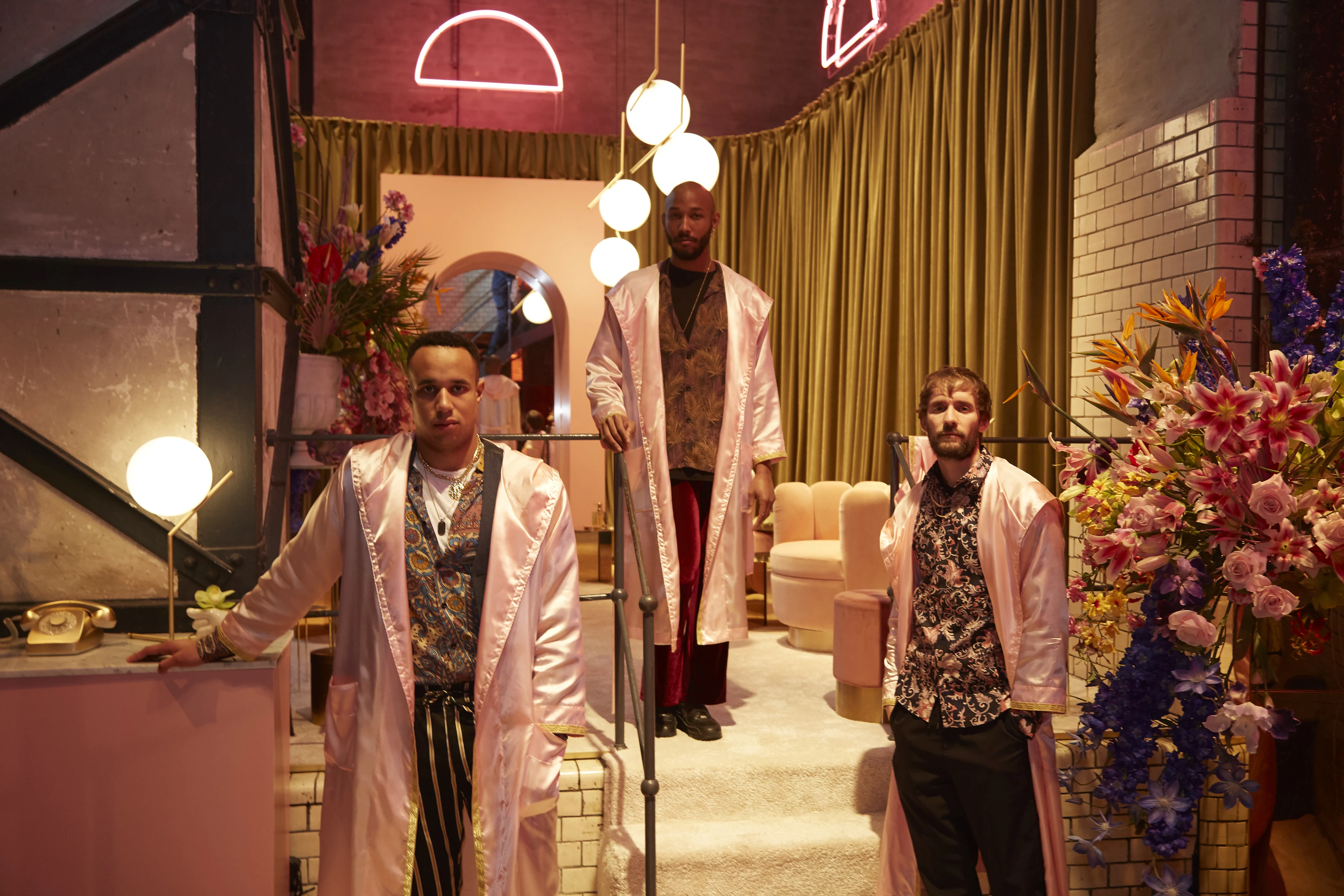 Three models in shiny pink robes posing in the pastel set of the Klarna pop-up during Berlin Fashion Week.