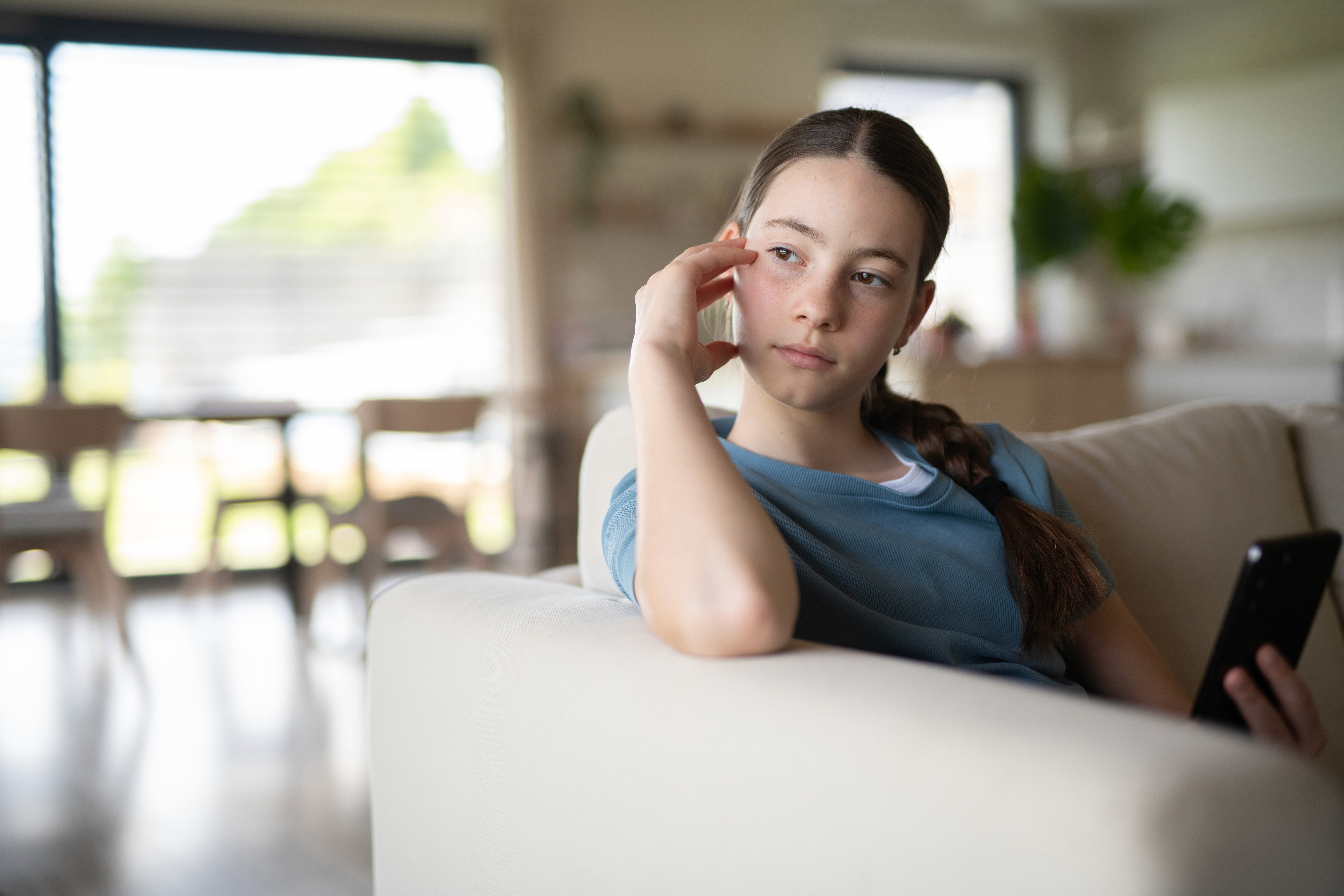 Modern open office lounge with large arched windows, plants, and soft round seating in white and terracotta tones, with people walking and working on laptops.