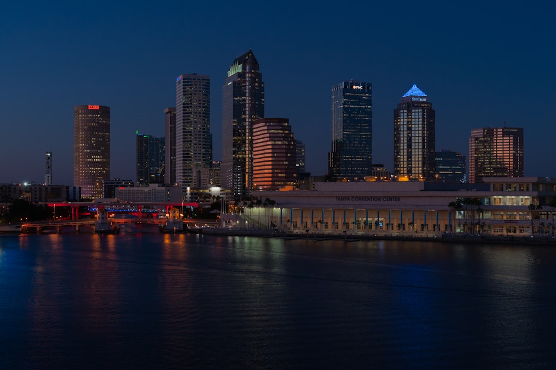 Illuminated city skyline with high-rise towers reflecting on calm waterfront at night.