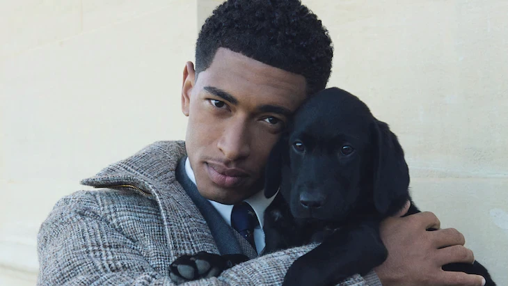 Man dressed in dark casual wear sitting alone in a stadium’s empty rows of purple chairs, lit by dramatic moody lighting.