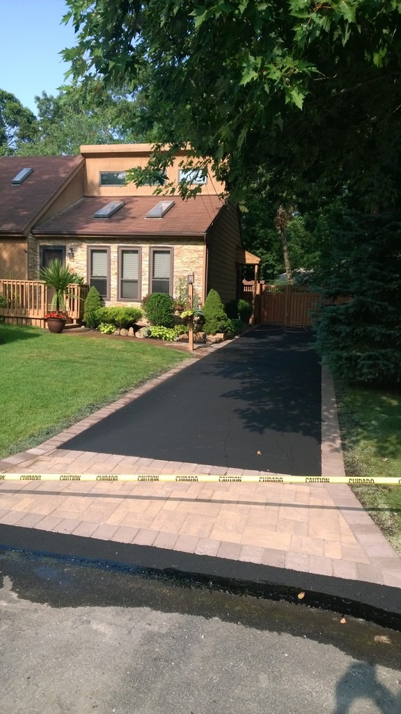 Newly paved asphalt driveway with stone border in front of suburban home