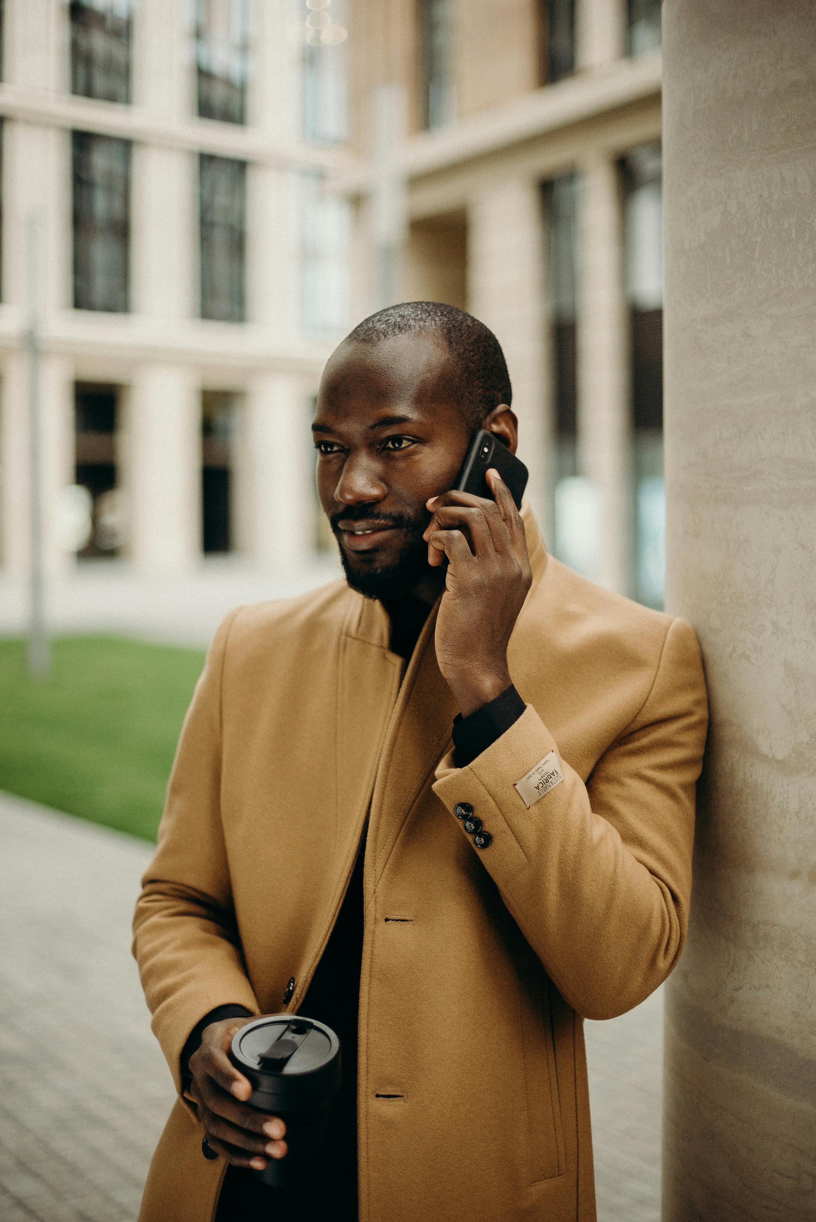 A man talking on the phone while leaning against the side of an office building