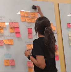 A portrait of woman with dark hair wearing stylish sunglasses, resting her chin on her hand against a plain background.