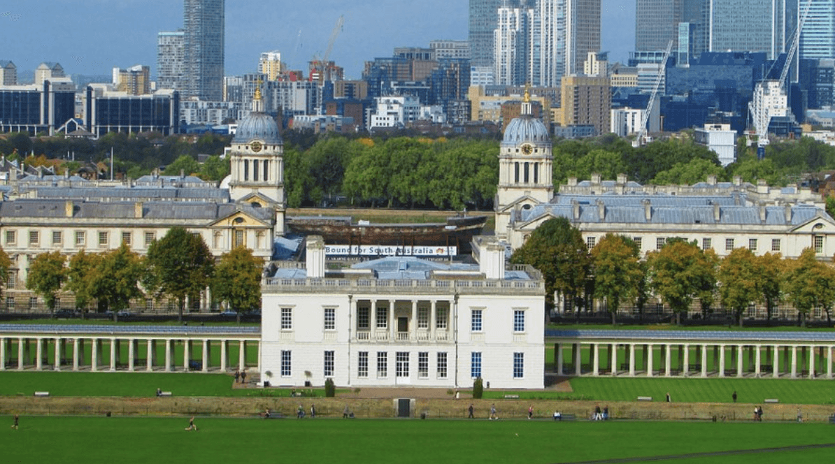 A smiling man with curly hair is sitting at a desk, looking at the camera, with a laptop and a lamp in the background.