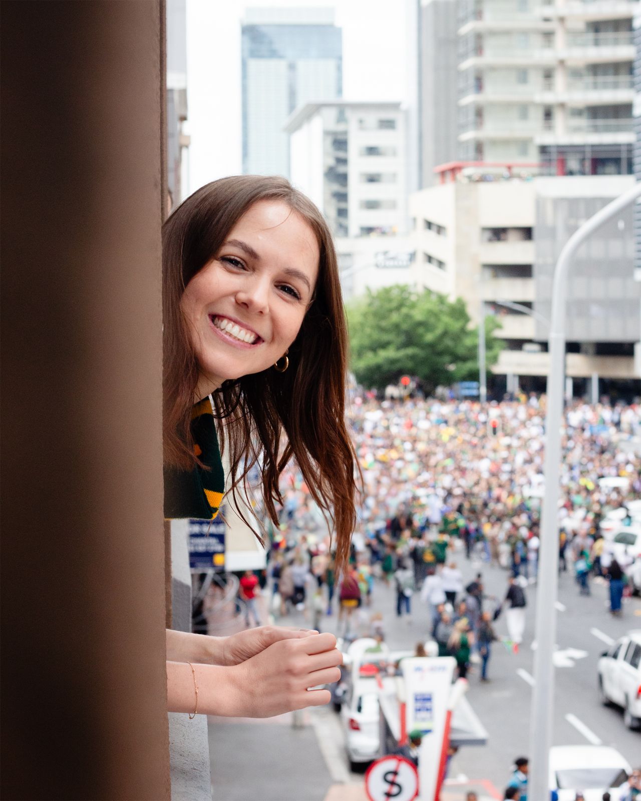 Smiling Cue crew member looking out at a large crowd in a city street from a high vantage point.